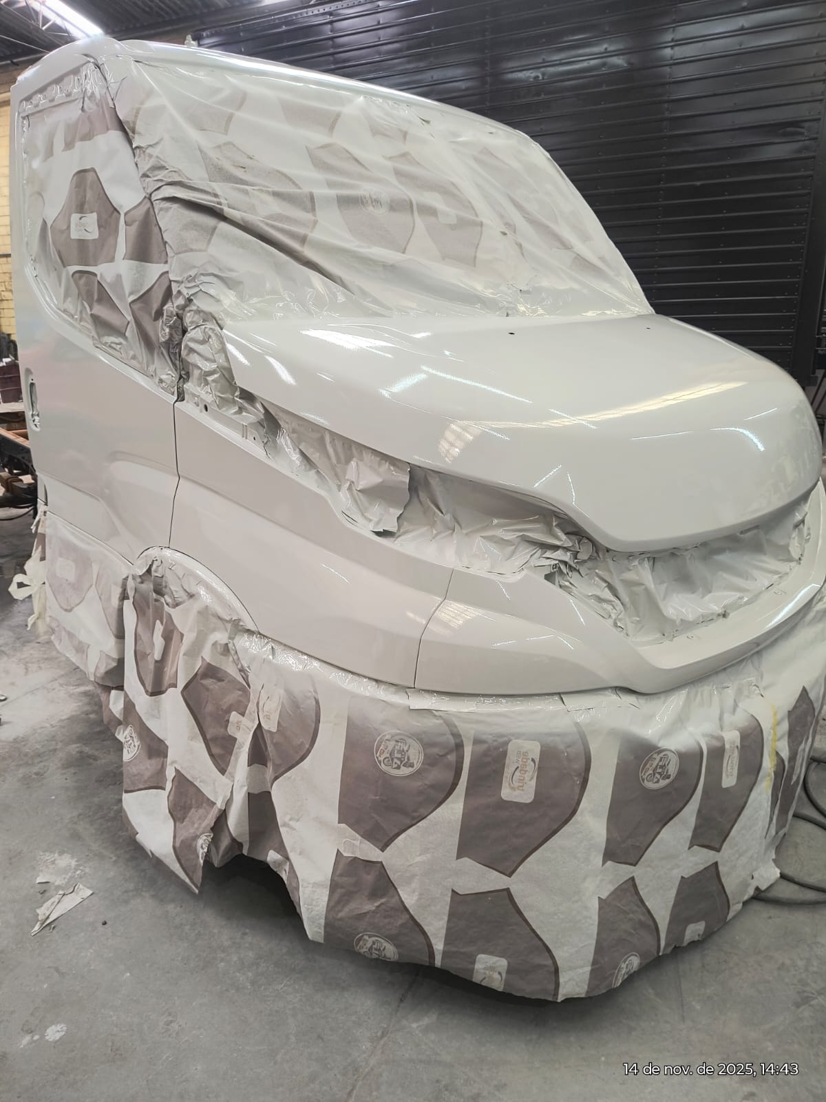 van sendo pintada de branco em oficina, com carroceria coberta por plástico de proteção