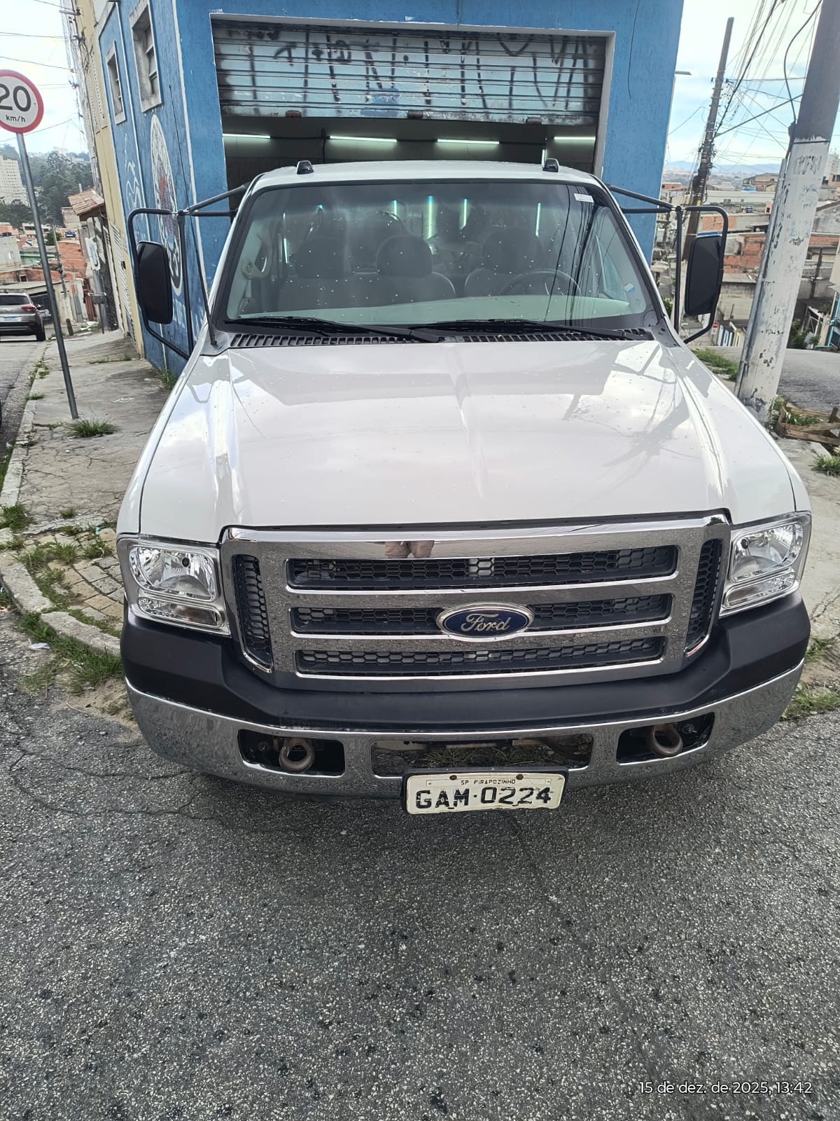 caminhonete Ford branca parada na frente de uma garagem azul numa rua ladeira