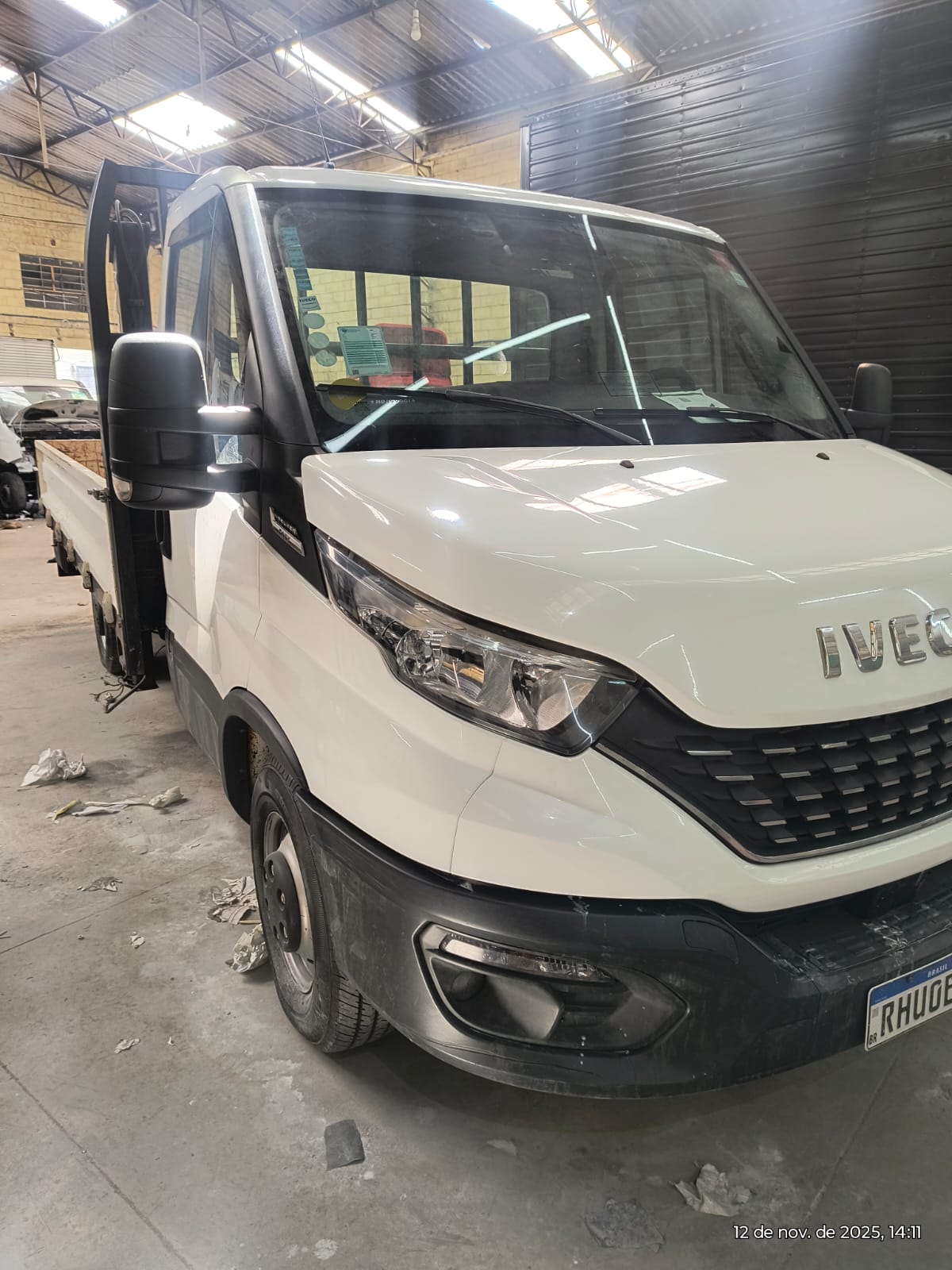 caminhão Iveco branco de carroceria aberta dentro de um galpão, placa RHU0B, com data 12 de nov. de 2025 no ca